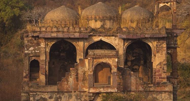 Weathered stone pavilion with arched openings amid dry scrub landscape in Rajasthan.