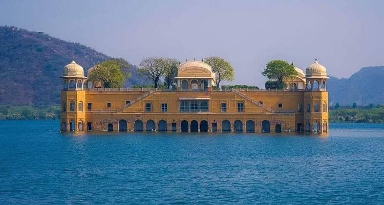The Jal Mahal palace sits serenely in the middle of Man Sagar Lake with hills behind.