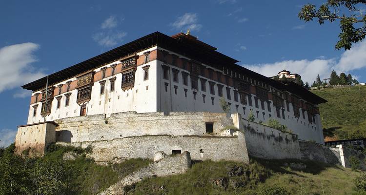 Side view of Paro Dzong's fortress walls rising above grassy embankment against blue sky.