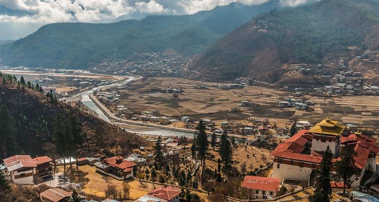 Wide valley view over Paro with patchwork fields, winding river and traditional buildings.