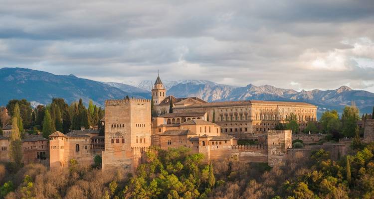 El majestuoso complejo del palacio de la Alhambra se alza sobre una colina boscosa con las nevadas montañas de Sierra Nevada al fondo.