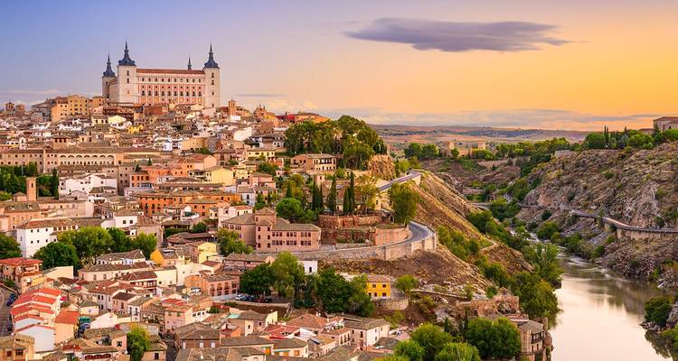Ciudad histórica de Toledo en la cima de la colina brillando al atardecer con el Alcázar dominando los tejados agrupados y una garganta de río sinuosa.