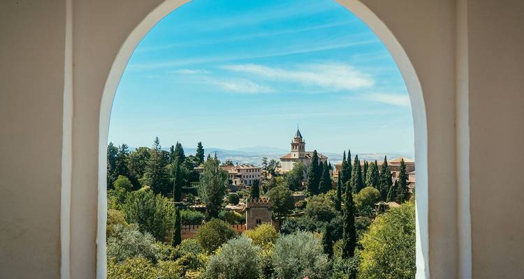 Door een gewelfd raam zie je een rustig uitzicht op het Alhambra van Granada, omgeven door cipresssen.