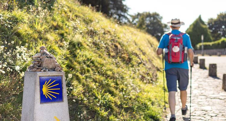 Marcador de piedra del Camino de Santiago con concha amarilla mientras un peregrino camina adelante