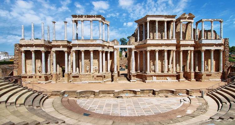 Teatro romano antiguo con gradas de piedra y escenario con columnatas bajo un cielo brillante