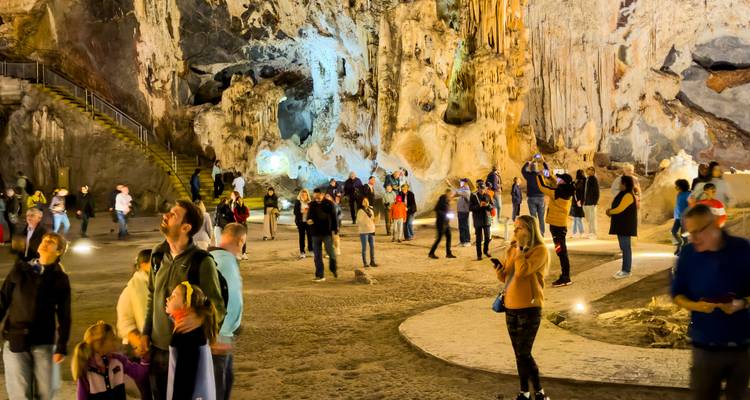 Touristen erkunden eine beleuchtete Kalksteinhöhlenkammer mit dramatischen Felsformationen