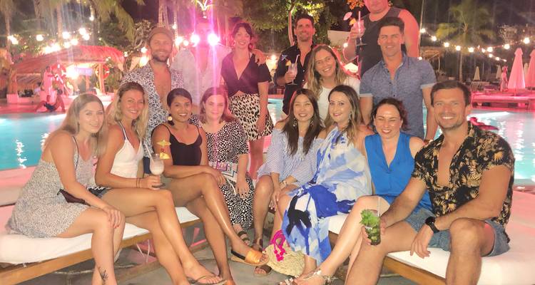Grupo de jóvenes viajeros posando con sonrisas al lado de una piscina iluminada en una reunión festiva por la noche