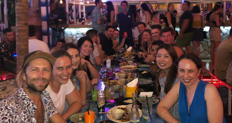 Mesa comunal grande donde viajeros disfrutan la cena juntos en un ambiente animado de mercado nocturno