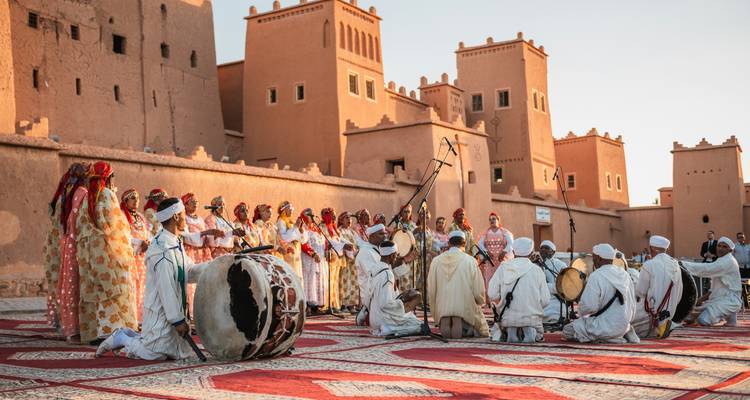 Traditional musicians and dancers perform in colorful dress before an adobe kasbah at golden hour