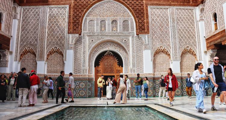 Ornate tiled courtyard of a Moroccan madrasa bustling with tourists around a central pool