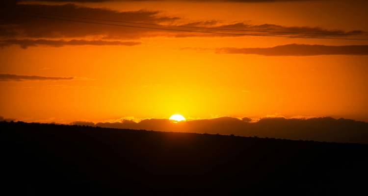Vibrant orange sun setting behind distant hills with silhouetted clouds