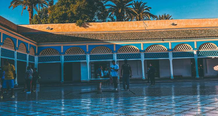 Visitors stroll through the tiled courtyard of Bahia Palace adorned with blue arches and palm trees above