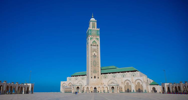 The Hassan II Mosque stands majestically under a clear blue sky in a vast open plaza
