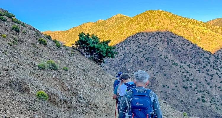 Les randonneurs suivent un étroit sentier de crête baigné dans la lumière chaude du soir à travers les montagnes de l'Atlas.