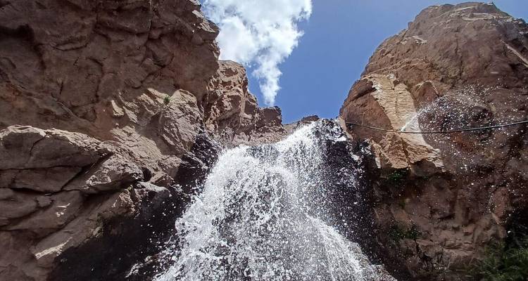 Une puissante cascade de montagne s'écoule avec force sur des rochers sombres dans une gorge étroite sous un ciel lumineux.