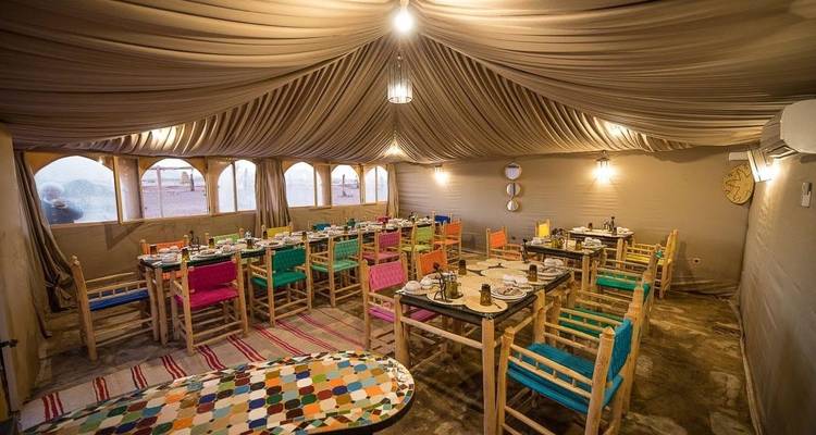 Tienda espaciosa de campamento en el desierto con sillas coloridas y mesas de comedor cuidadosamente dispuestas esperando a los huéspedes.