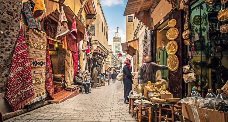 Ruelle colorée dans une médina marocaine bordée de tapis suspendus, de boutiques de cuivrerie et d'habitants locaux.