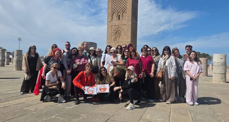 Grand groupe de touristes posant avec des panneaux devant la Tour Hassan et des colonnes de marbre sous un ciel bleu.