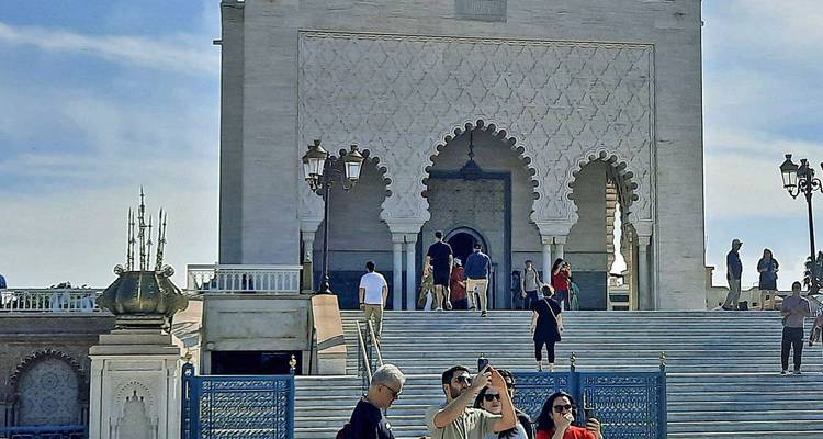 Les visiteurs prennent des photos sur le grand escalier du mausolée de Mohammed V avec des arches blanches ornées derrière.