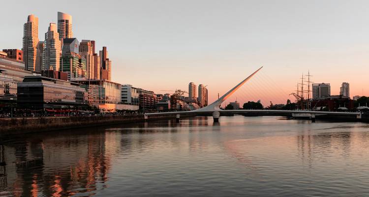 The skyline of Buenos Aires with a modern bridge and calm waters during sunset.