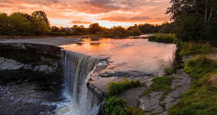 A small waterfall flowing into a river during sunset.