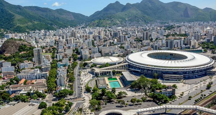 An aerial view of a large stadium and surrounding city with mountains.