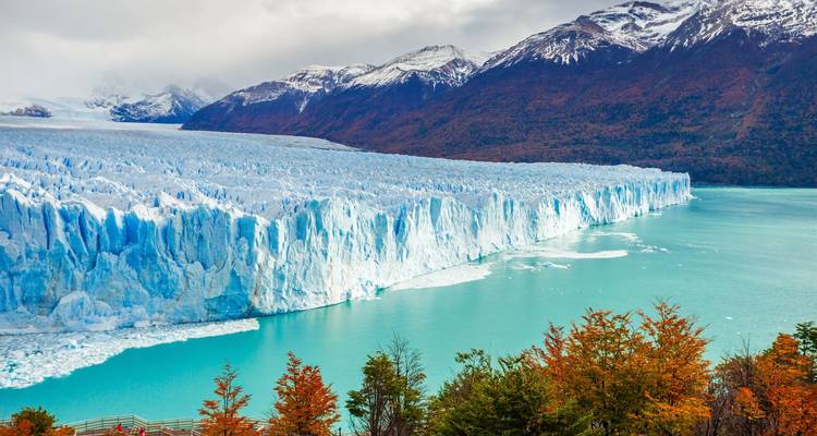Glacier meeting a turquoise lake with autumn-colored trees.