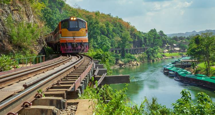 Train panoramique traversant un pont au-dessus d'une rivière dans un paysage luxuriant.