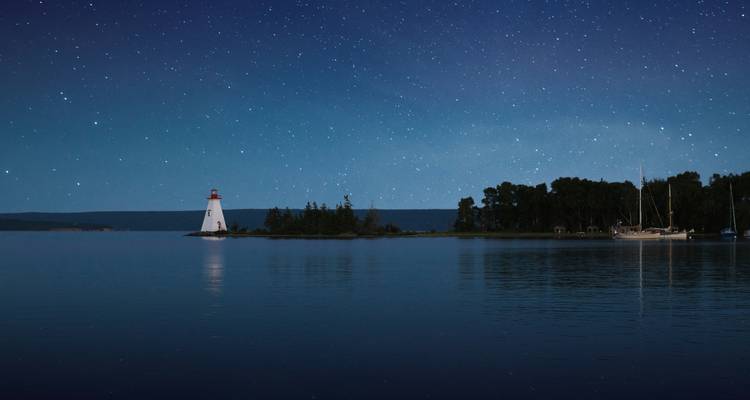 Lighthouse by the sea under a starry night sky.