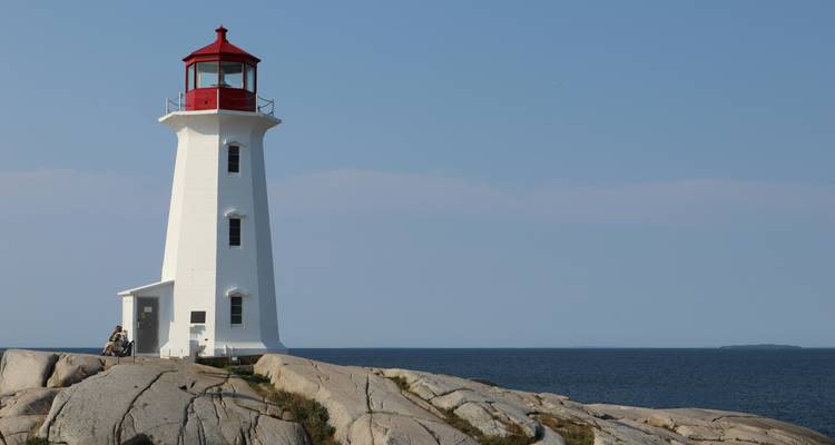 Lighthouse on rocky cliffs with blue sea and sky.