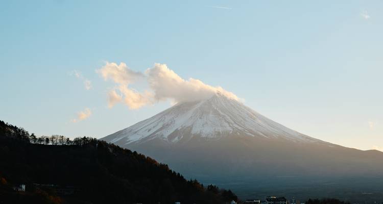 Mount Fuji bedekt met sneeuw en een pluim van wolk onder helder avondlicht