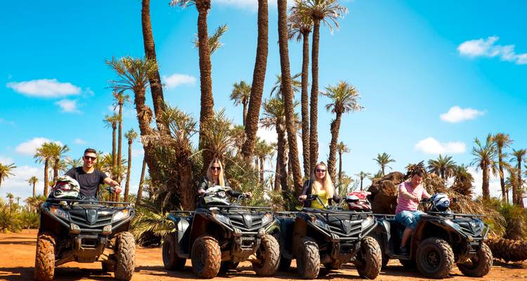 Four people riding quad bikes among palm trees in a desert landscape.