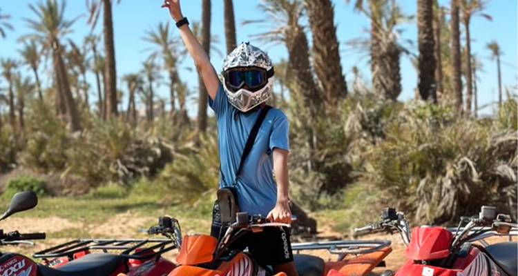 Person on a quad bike raising hand in a desert with palm trees.
