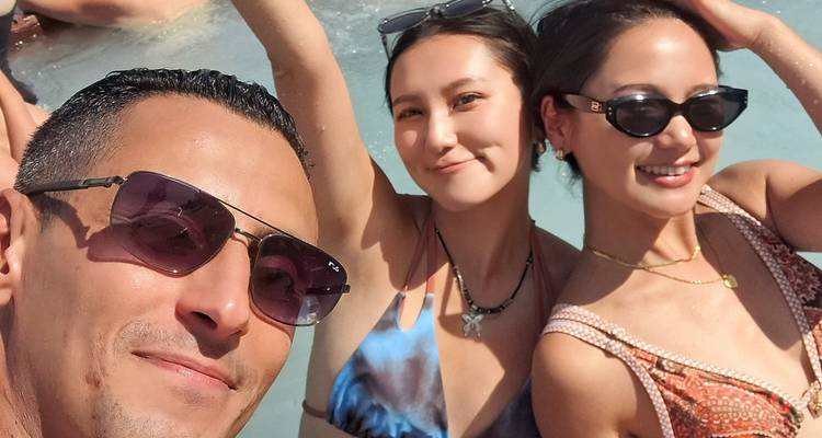 Trois amis en maillot de bain sourient pour un autoportrait rapproché tandis qu'ils se détendent dans une piscine turquoise.