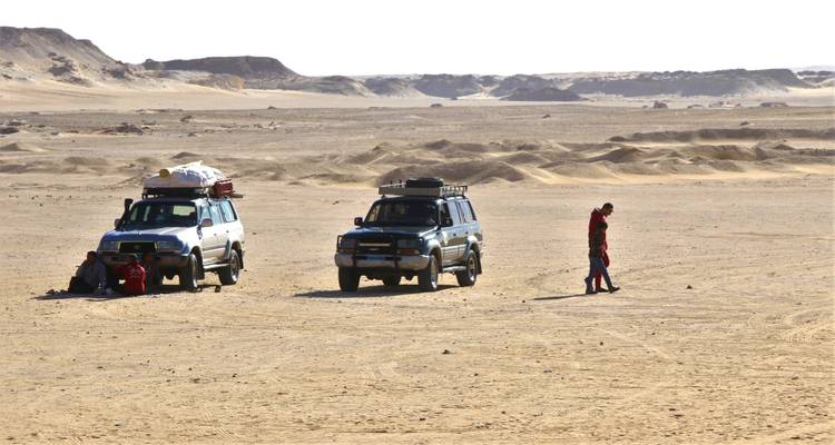 Deux jeeps et un voyageur solitaire se dressent au milieu des ondulations du sable et des crêtes rocheuses du désert ouvert.