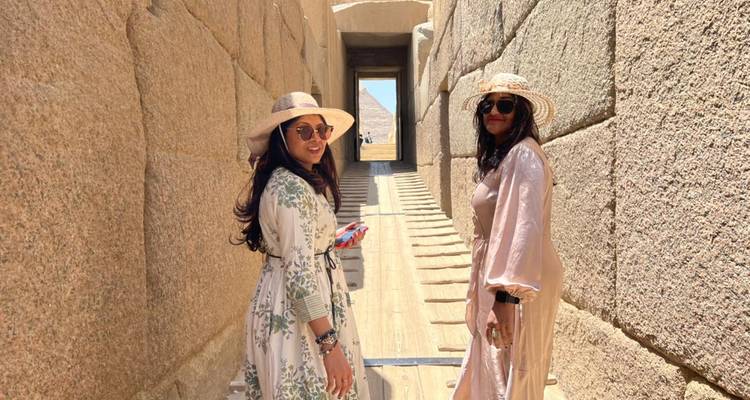 Deux femmes portant des chapeaux de soleil se promènent dans un passage en pierre étroit à l'intérieur d'un complexe pyramidal ancien.
