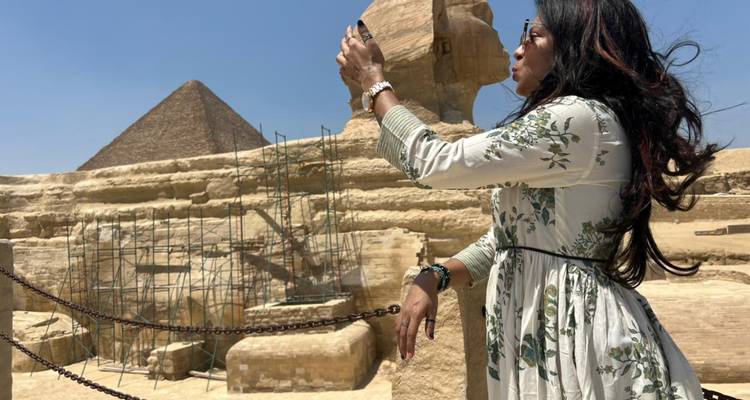 Une femme photographie le Sphinx avec la Grande Pyramide s'élevant derrière des échafaudages de restauration.