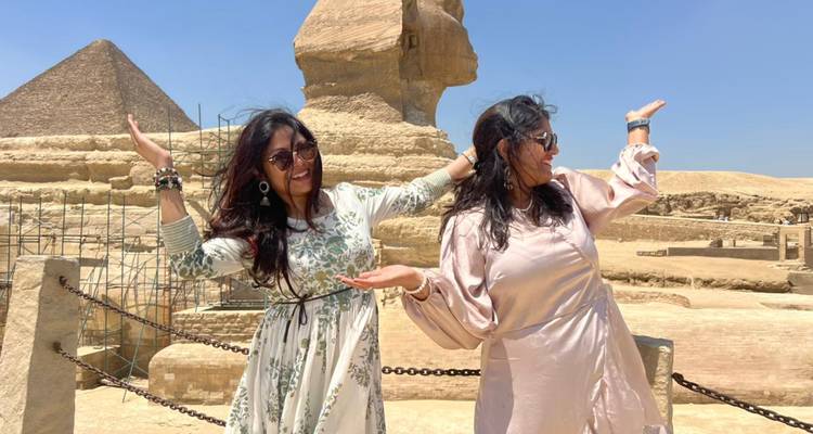 Deux femmes posent de manière ludique devant le Sphinx, les bras écartés, avec les pyramides en arrière-plan.