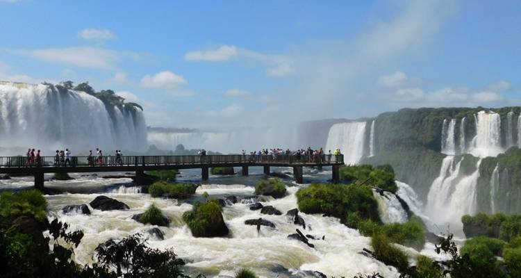 Tourists stand on a walkway surrounded by misty curtains of Iguazu Falls