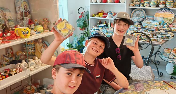 Tres chicos muestran con orgullo baldosas de limón pintadas a mano dentro de una colorida tienda de cerámica.