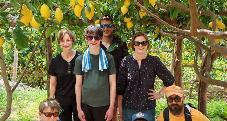 Una familia posa bajo una arboleda de limones sombreada rodeada de frutas amarillo brillante y hojas verdes.