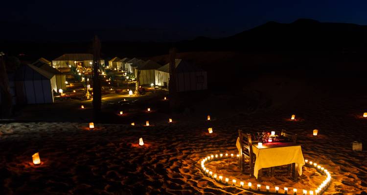 A candle-lit desert camp at night with a romantic setup.