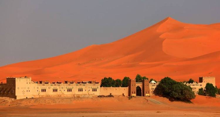 A desert kasbah with sand dunes under a clear sky.