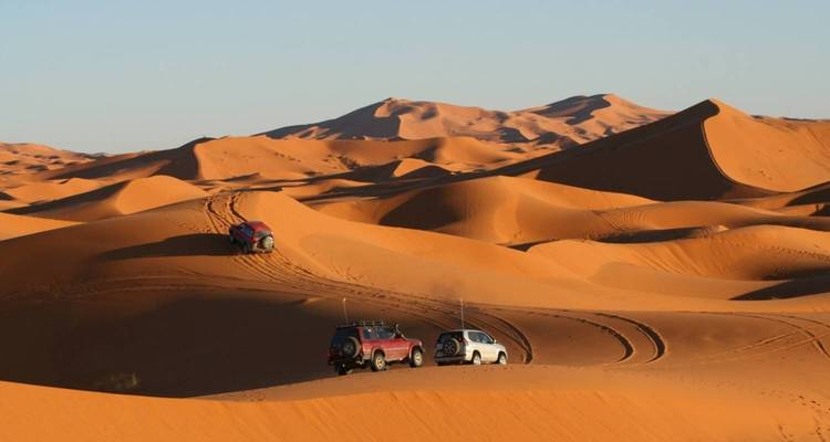 A desert landscape with vehicles leaving tracks on sand dunes.