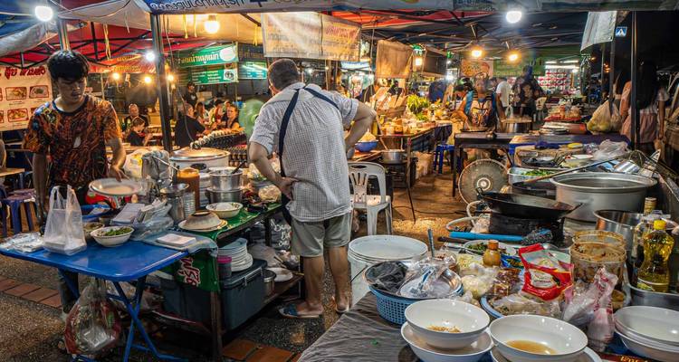 Marché de street food animé avec des vendeurs qui cuisinent et servent de la nourriture.