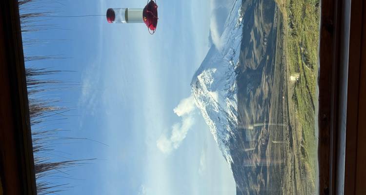 Vista de montaña a través de una ventana con un comedero para colibríes.