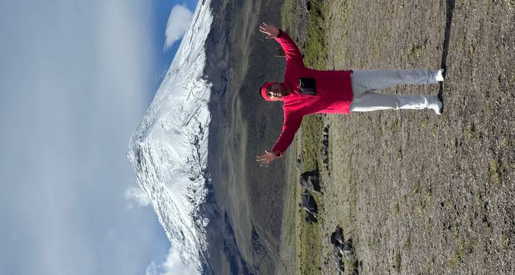 Persona posando con los brazos levantados frente a una montaña nevada.