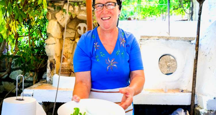 A woman presenting a dish in a traditional kitchen setting.