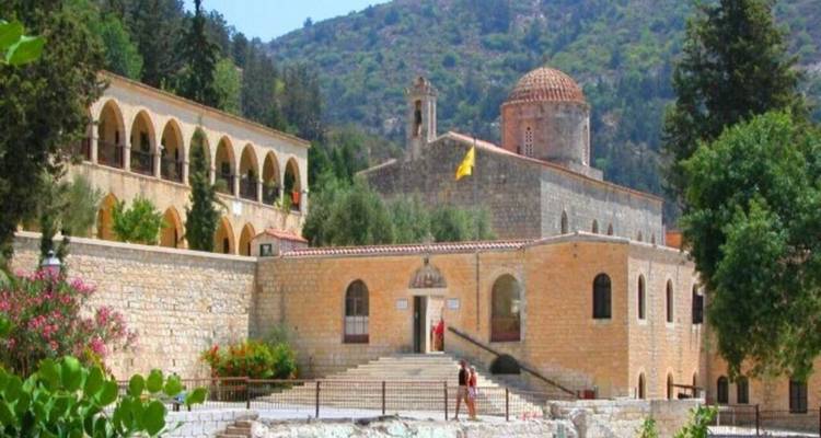 Mountain monastery with arches, domed church and yellow flag set against forested slopes