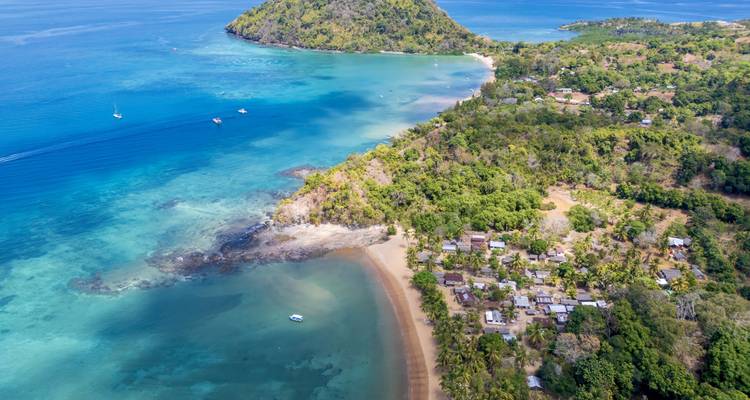 Vista aérea de una península verde, aguas azul turquesa y un pequeño pueblo costero en Nosy Be.